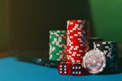 Fichas de cassino e dados sobre uma mesa de feltro ao lado de um laptop, representando apostas online.