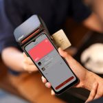 Close de um smartphone realizando pagamento por aproximação em um terminal de cobrança.