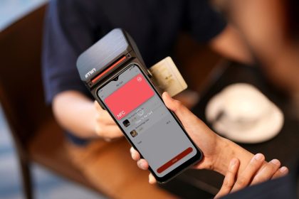 Close de um smartphone realizando pagamento por aproximação em um terminal de cobrança.