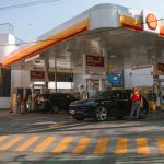 Posto de combustíveis com carros abastecendo e frentistas atendendo os motoristas durante o dia.