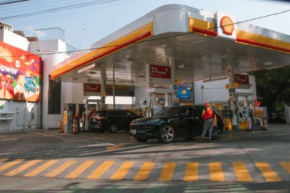 Posto de combustíveis com carros abastecendo e frentistas atendendo os motoristas durante o dia.