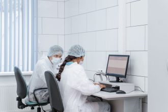 Dois cientistas analisam dados juntos em um computador dentro de um laboratório.