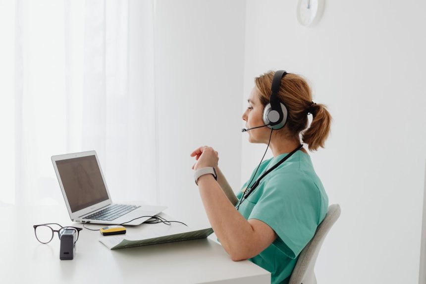 Médica participa de uma consulta on-line usando laptop e headset em um consultório.