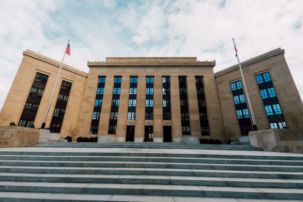 Exterior do prédio do Federal Reserve em Washington, com bandeiras dos Estados Unidos e escadaria sob céu nublado.