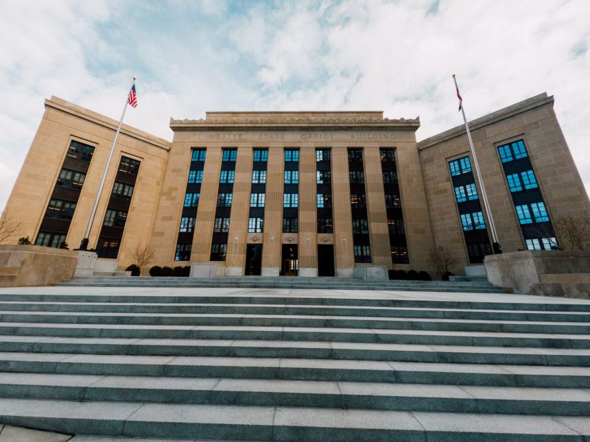 Exterior do prédio do Federal Reserve em Washington, com bandeiras dos Estados Unidos e escadaria sob céu nublado.